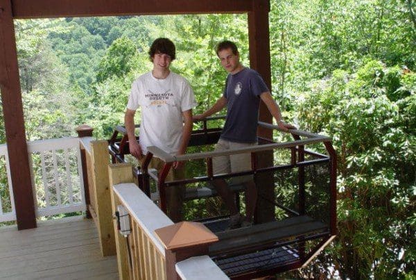 Hillside funicular lift parked at top of a covered upper landing area with wood railing and two riders on board the car